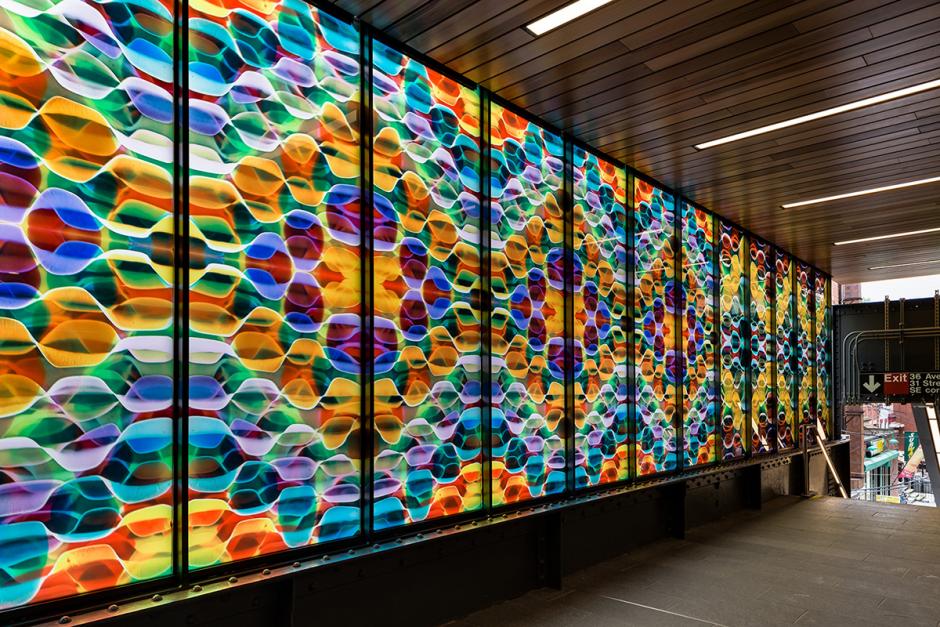 Photo of station mezzanine interior with Maureen McQuillan’s multicolored glass artwork on left and station exit stairs on right. 