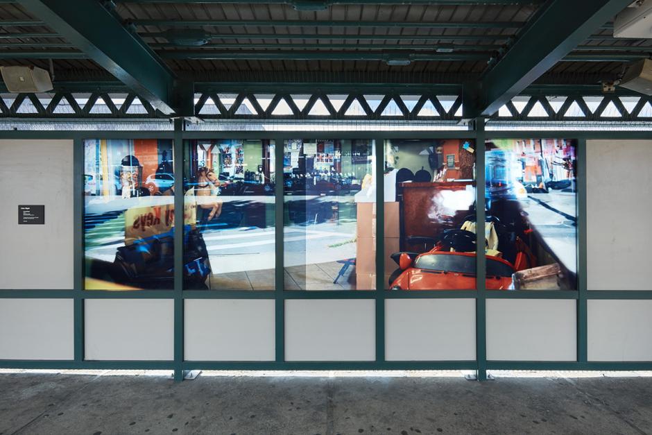 Photograph of laminated glass artwork on the platform walls of the Avenue N station in Brooklyn. The artwork shows a straight on shot of photography on glass showing surface reflections of the street and interiors as well as station reflections.