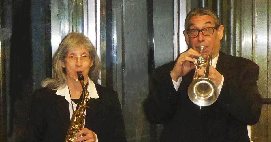 Man playing trumpet and woman playing saxophone in suits.