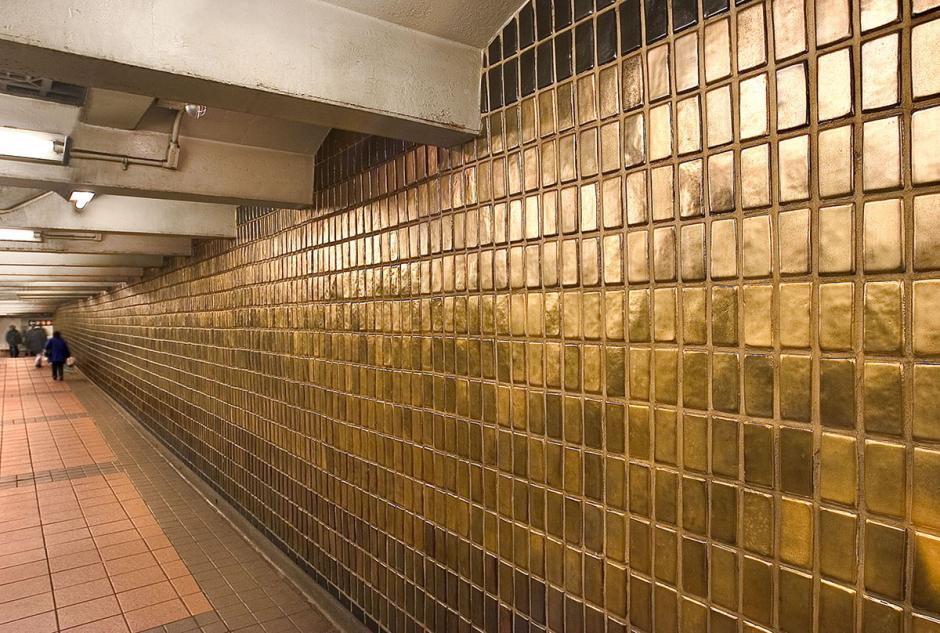 Artwork by Michele Oka Doner showing glowing bronze color tiles from floor to ceiling along the passageway. 