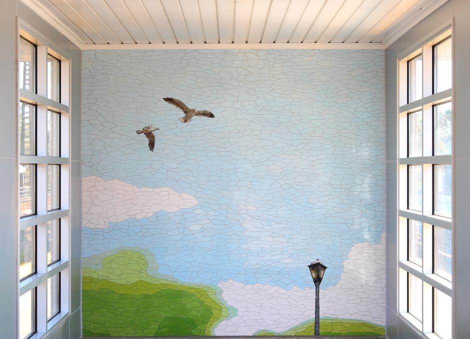 Artwork in glass and ceramic mosaic by Malin Abrahamson showing blue skies and green fields with birds and suburban scenes.