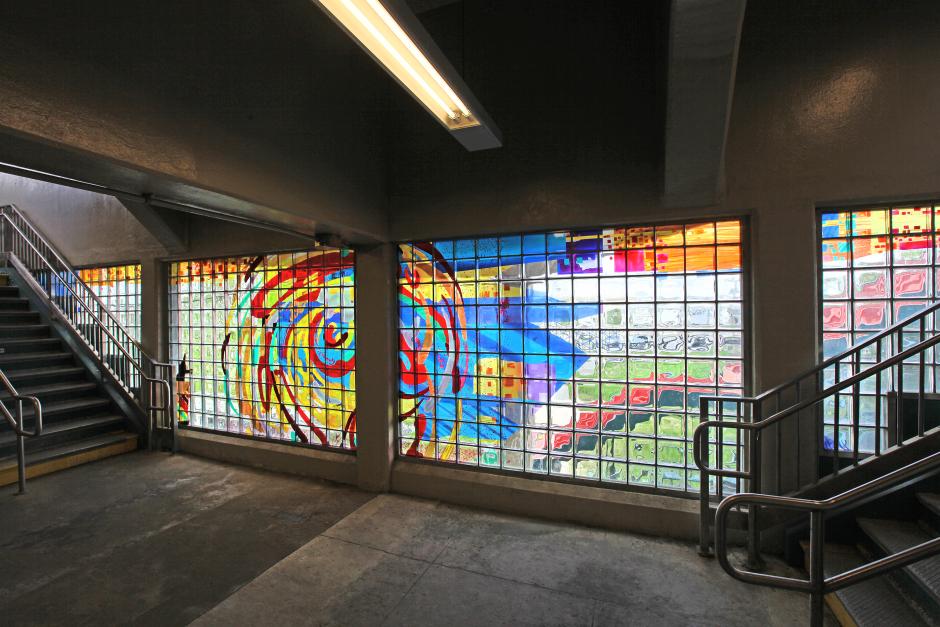 Artwork in glass block by George Bates showing colorful large circular forms and geometric patterns and a spiral of people’s heads formed by blue lines.