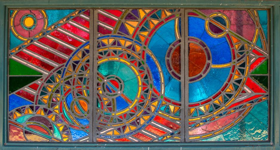 Artwork in faceted glass by Ellsworth Ausby showing eight colorful triptychs with swirling forms and abstract shapes in mezzanine windows and platform windscreens. 