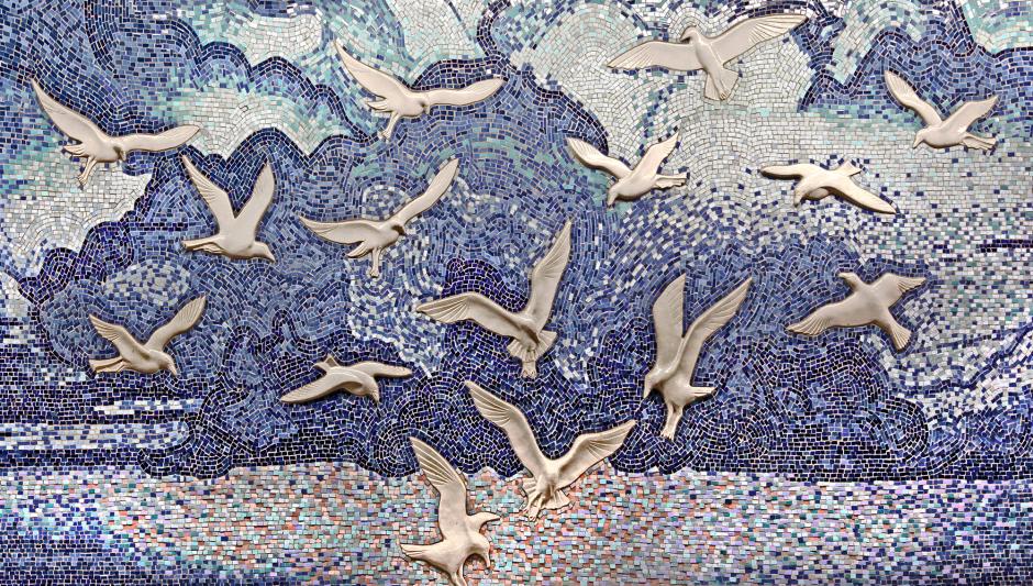 Artwork in handmade ceramic relief tiles, ceramic mosaic, cut granite floor tile, bronze, and forged steel by Frank Girorgini showing a cityscape, flora and fauna and seagulls.  