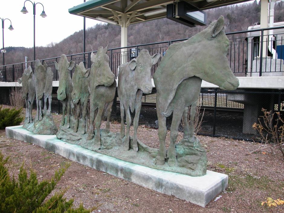 Artwork in cast bronze by Ann Huibregtse showing life size cows outdoors near the platform stairs.  