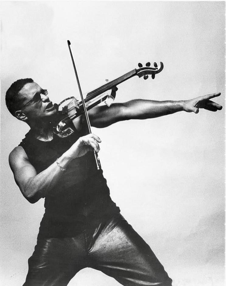 Man in leather pants, tank top and sunglasses playing violin.