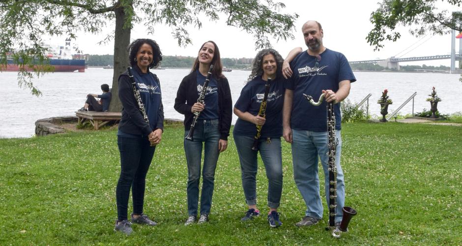 Three women and one man holding clarinets in a park.