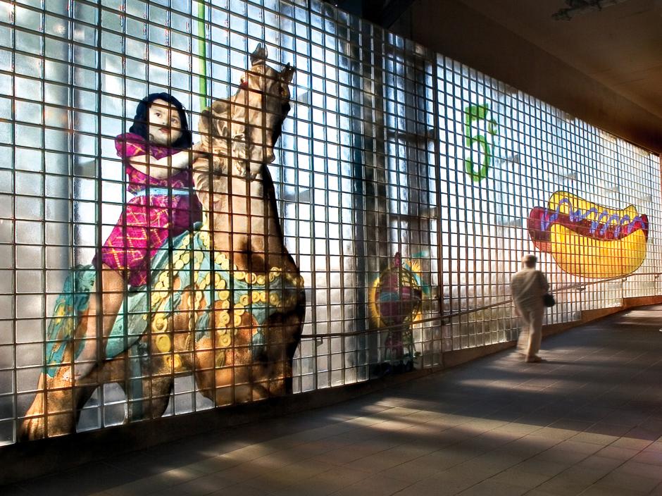 Artwork in glass block by Robert Wilson showing large colorful images of Coney Island scenes with people, roller coasters and an oversized hot dog.  