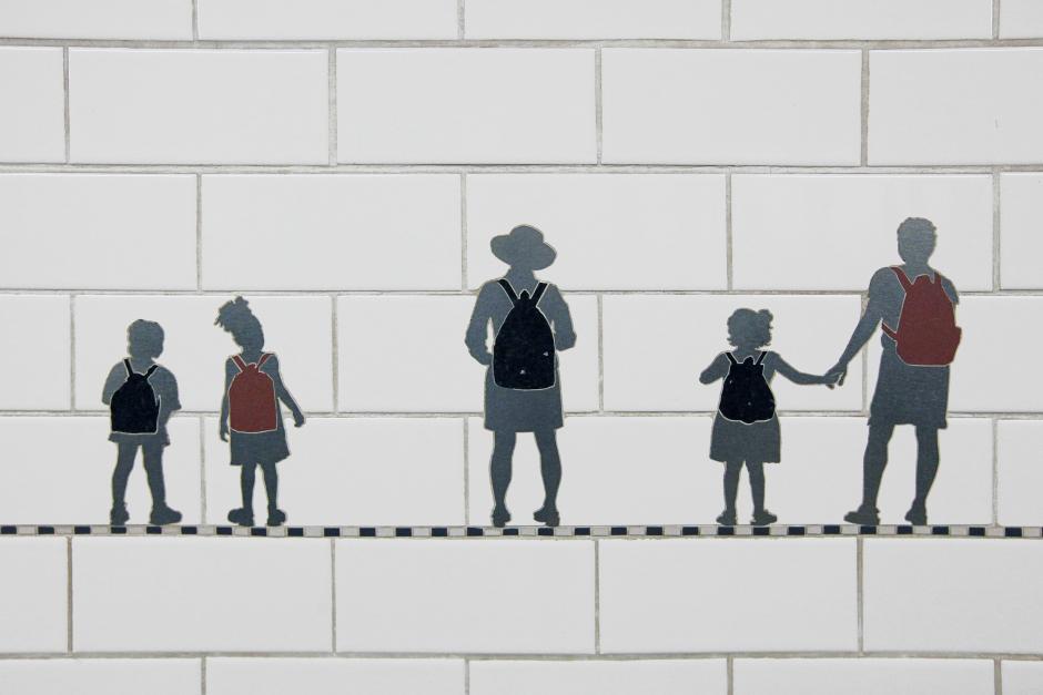 Artwork in steel, marble, and slate frieze on platform walls by Janet Zweig and Edward del Rosario showing almost two hundred small silver silhouettes of people hauling stuff with them as they walk the city streets. 