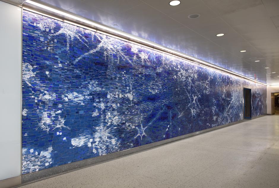 Mosaic artwork along a train station corridor, the mosaic depicts light as it hits a flowing blue river.