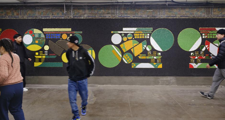 Artwork in ceramic mosaic by Glendalys Medina showing colorful geometric forms against a dark background along the platform wall. 