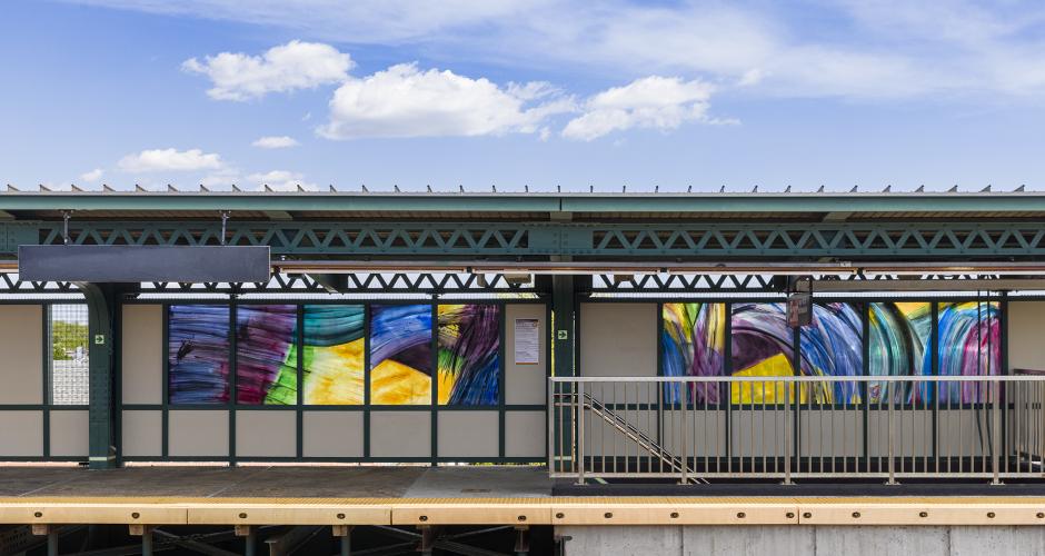 Elevated station platform with two sets of glass artworks featuring large brushstrokes in the windscreens. 