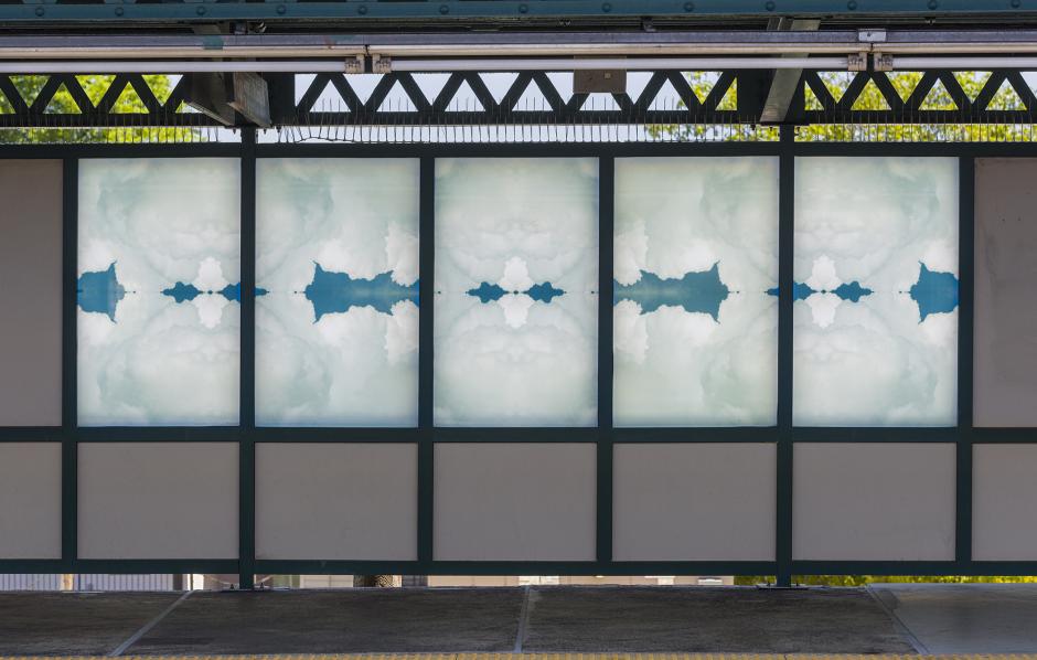 Glass artwork on an elevated station platform depicting kaleidoscopic images of clouds.