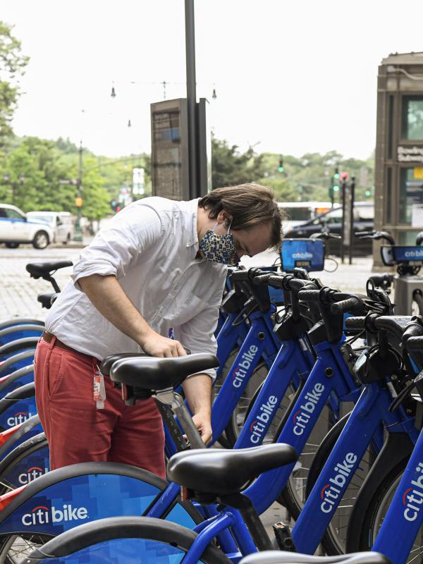 A man selects a blue Citi Bike from a bike-share station near a subway stop.
